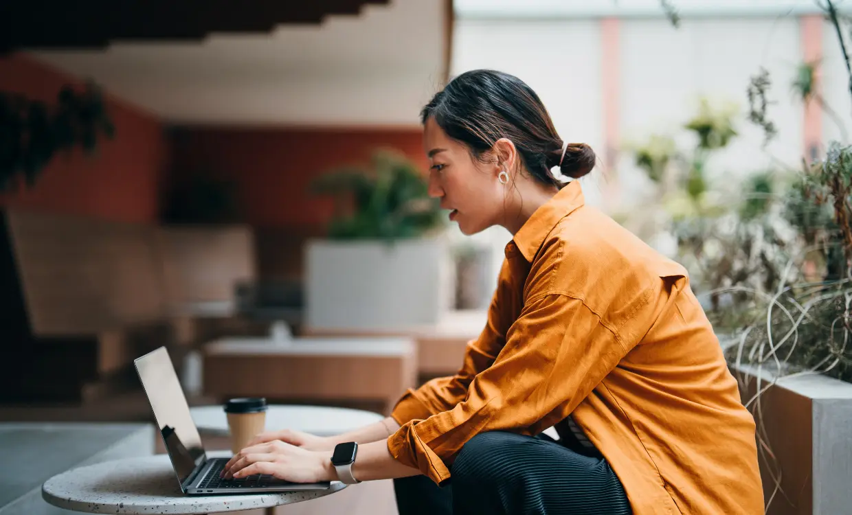 Woman types on her computer while sitting down with a cup of coffee