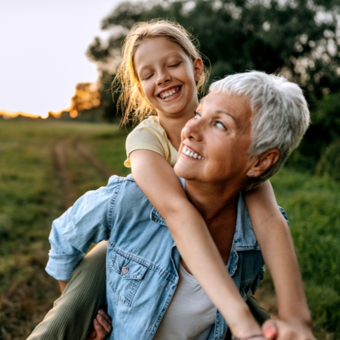 Older woman smiles while giving a young girl a piggyback ride