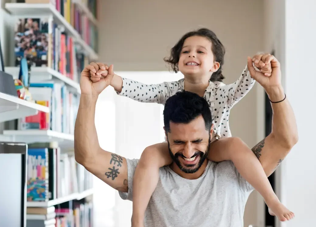 Young child smiles while on the shoulders of a man