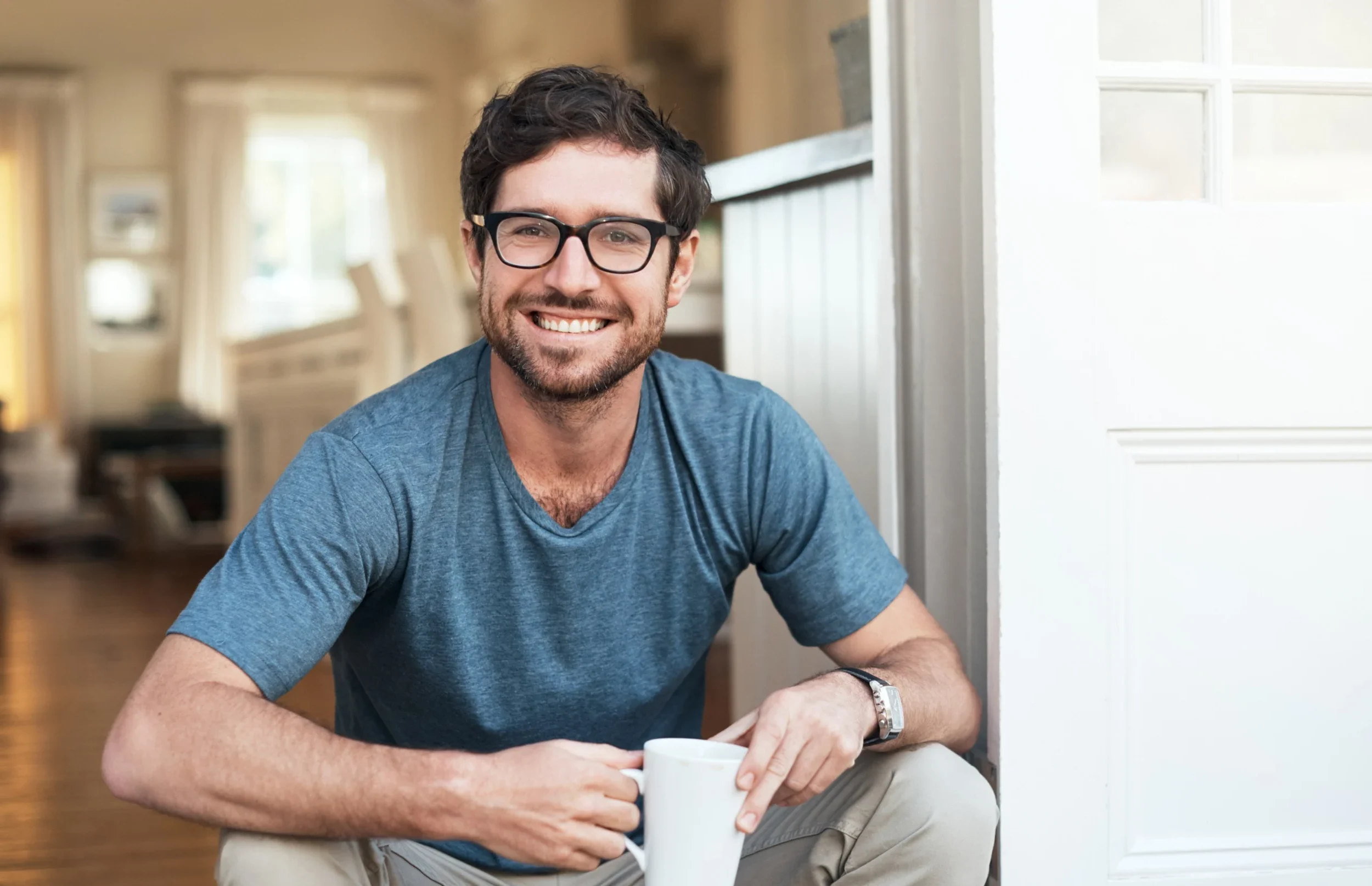 Man smiles at camera while enjoying a cup of coffee on the step of his home