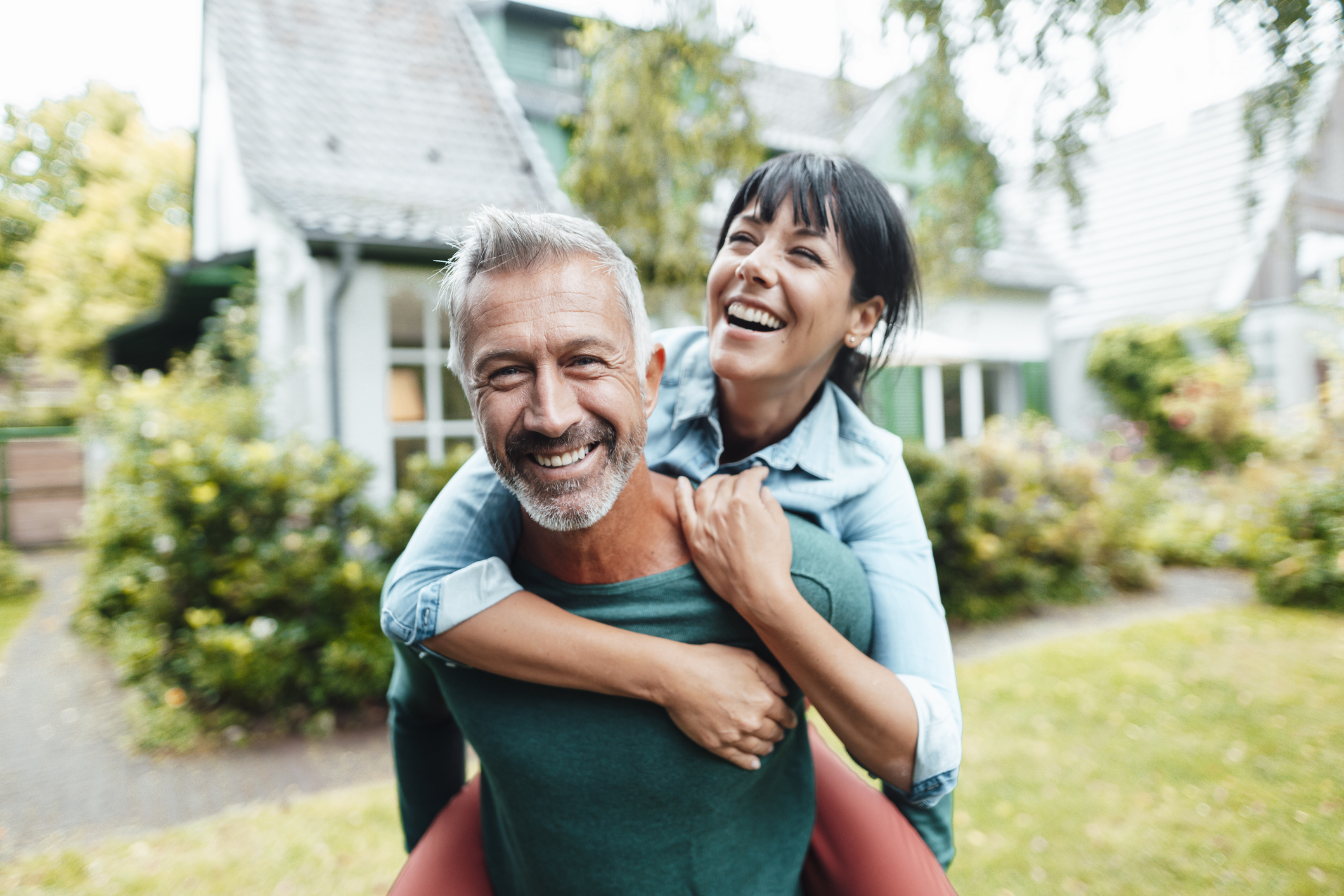 Man and woman smile while he gives her a piggyback ride in backyard