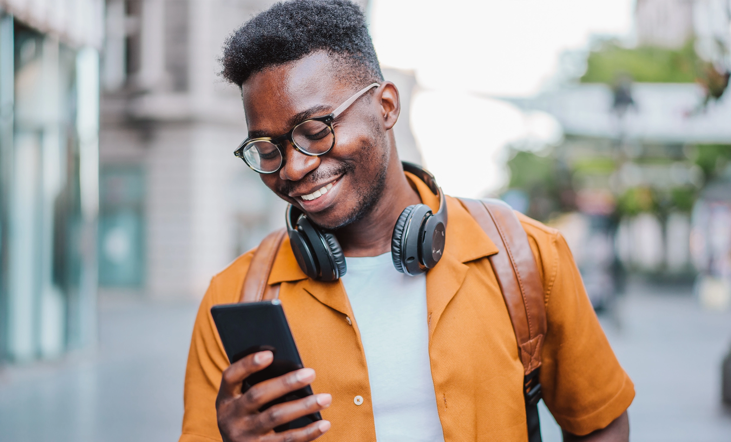 Man smiles at his phone while walking with a backpack