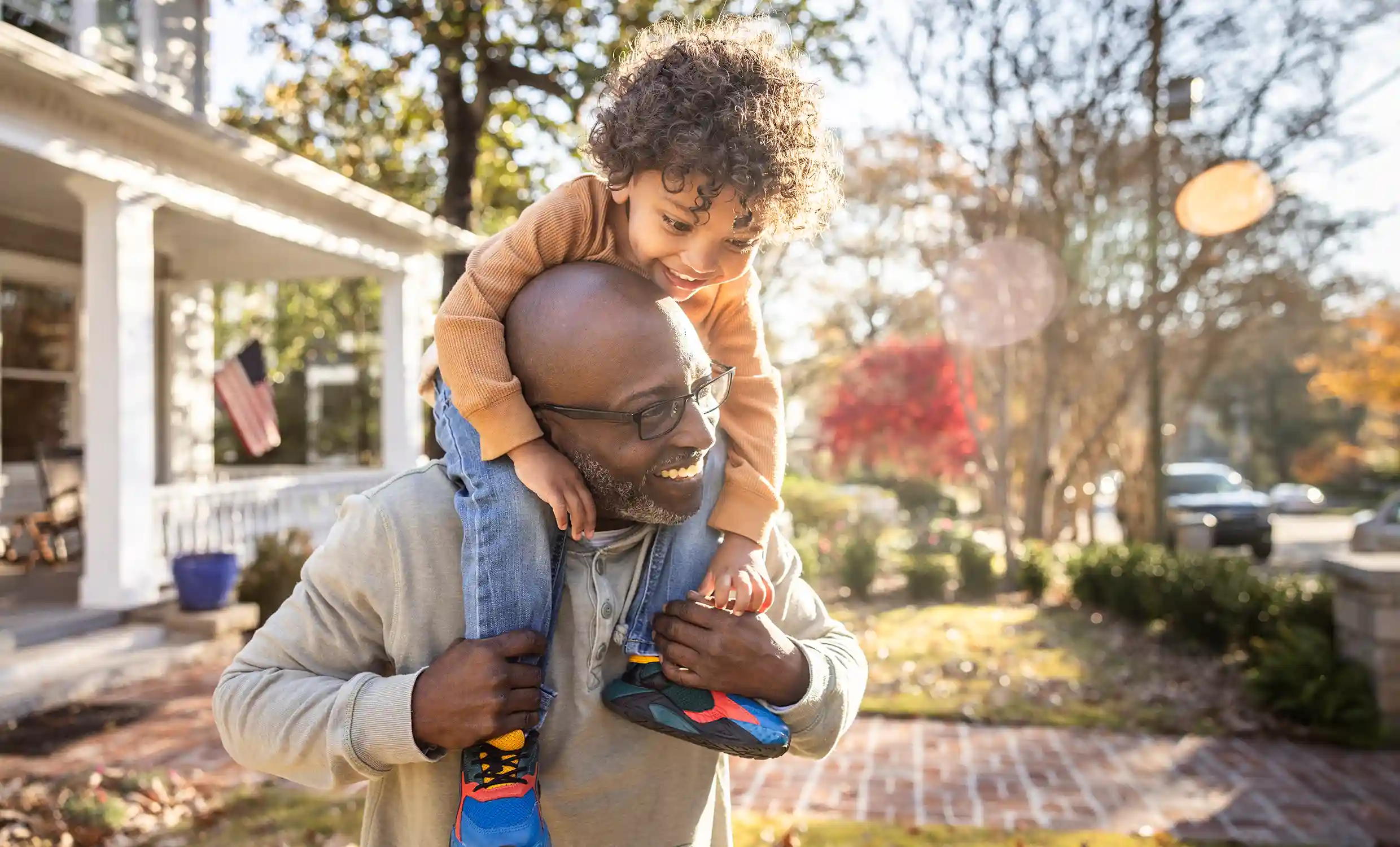 An African American man gives his son a piggy back ride in their front yard