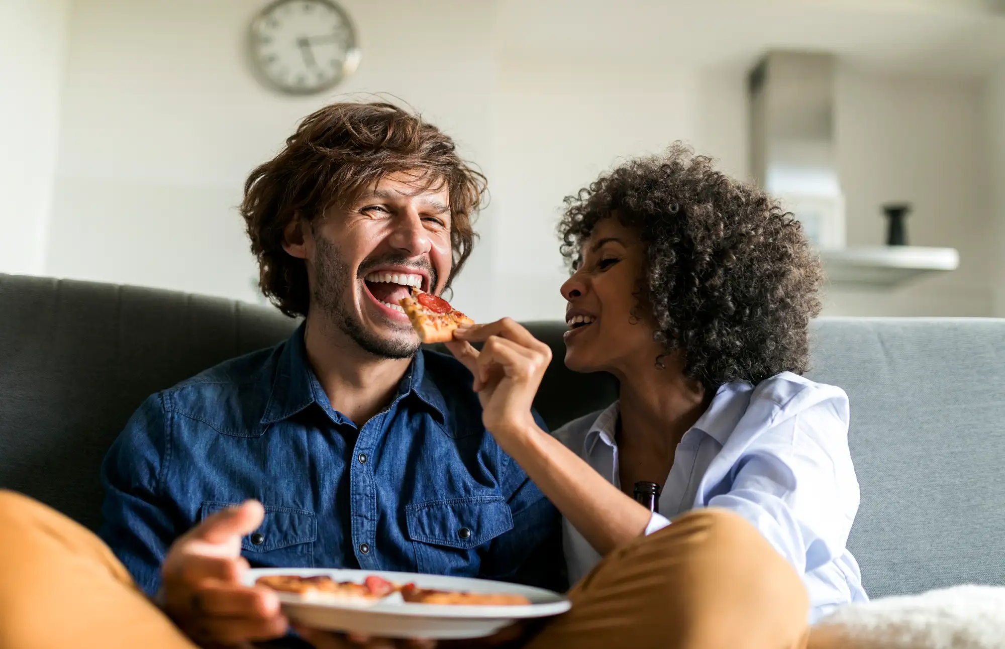 women feeding man pizza on the couch