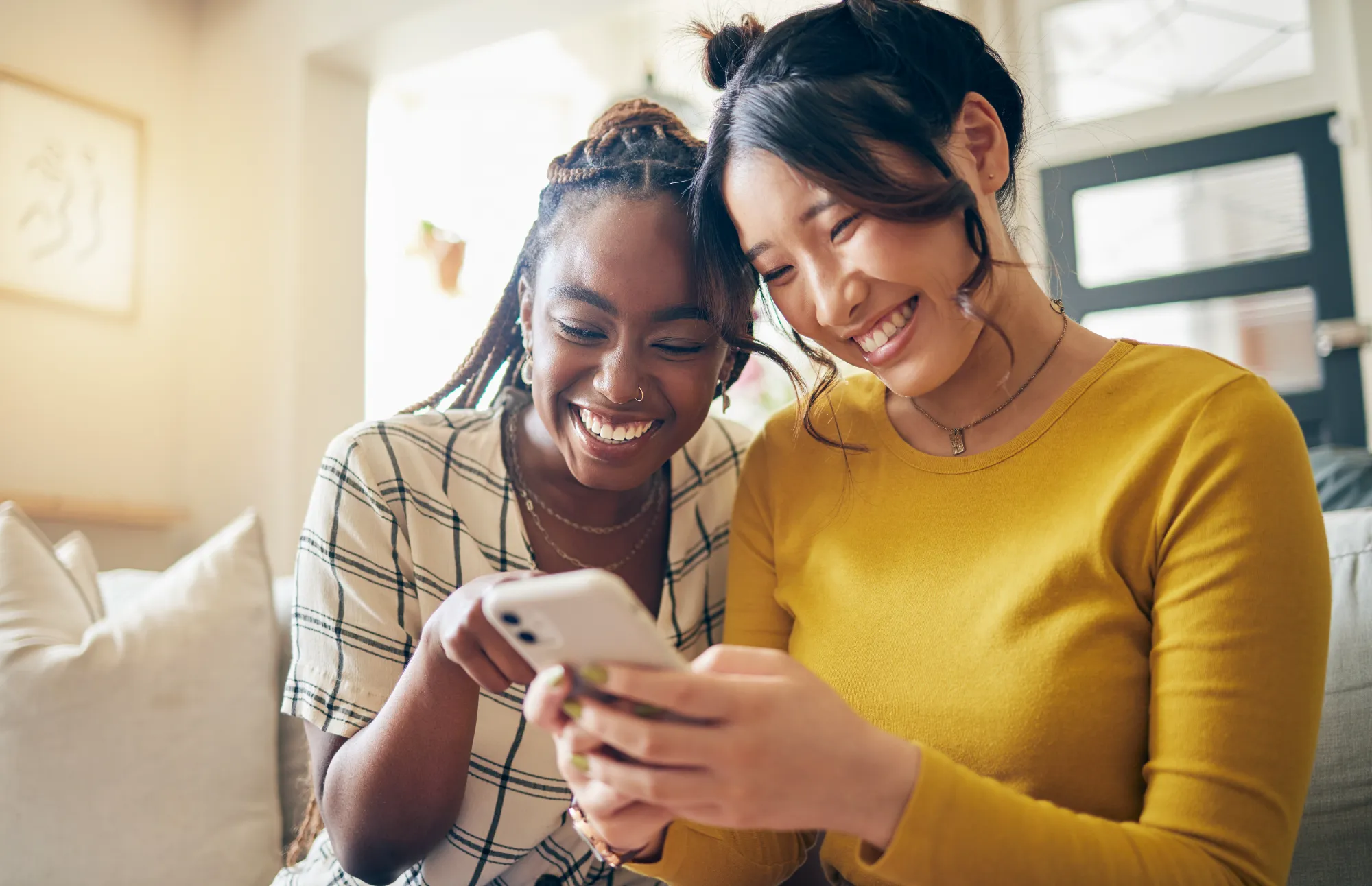 Two young women smiling and looking at a smartphone together.