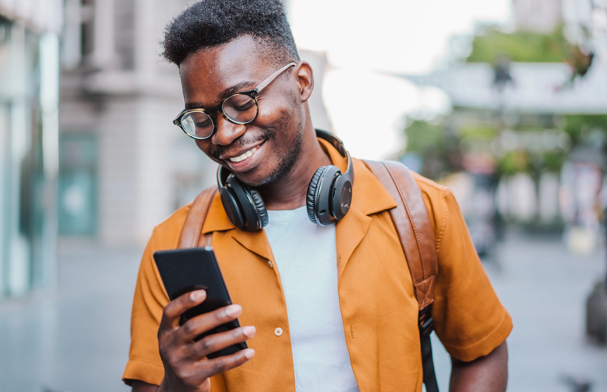 Man smiles at his phone while walking with a backpack on