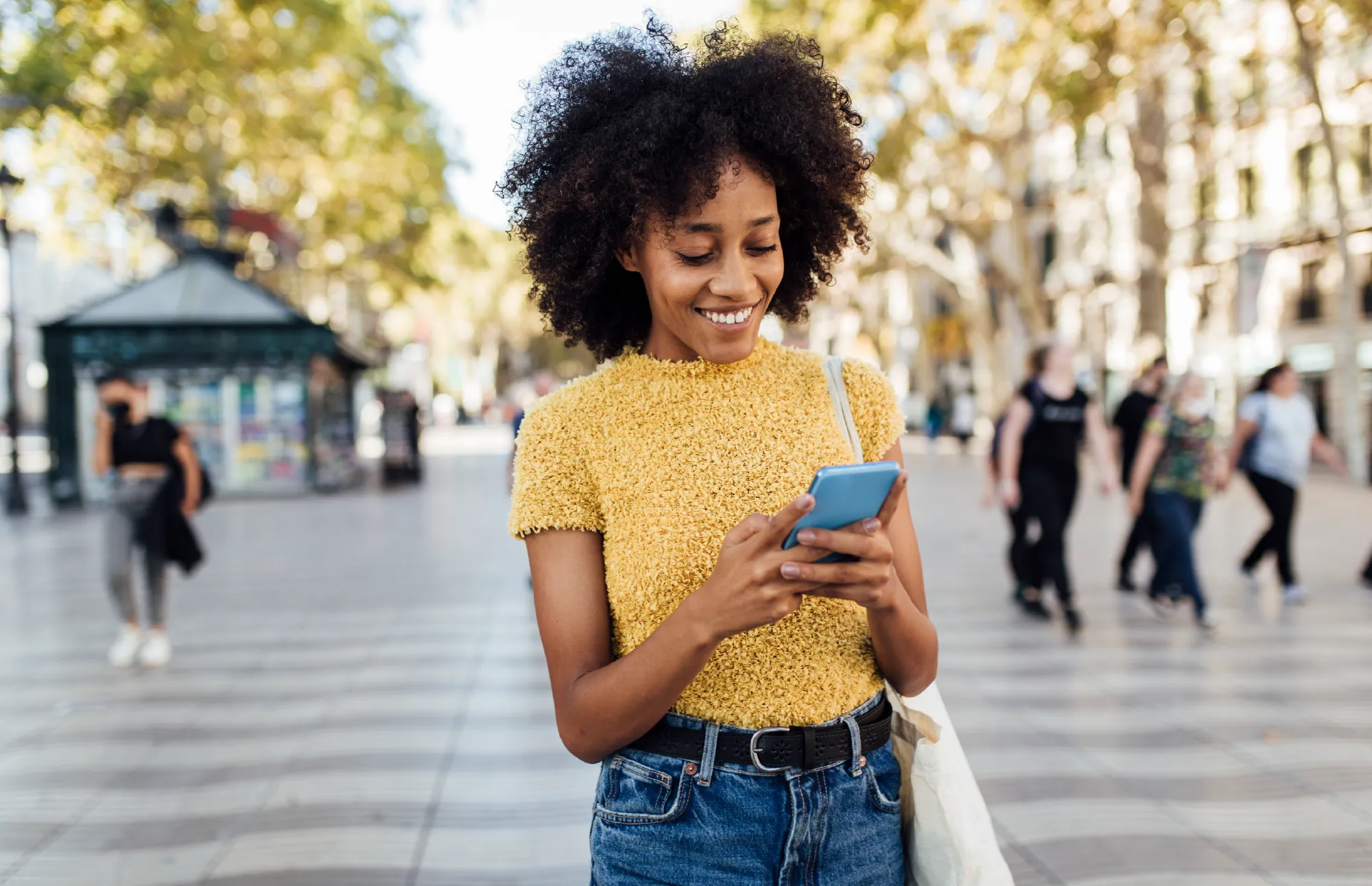 Woman smiling while using her phone outdoors on a city street.