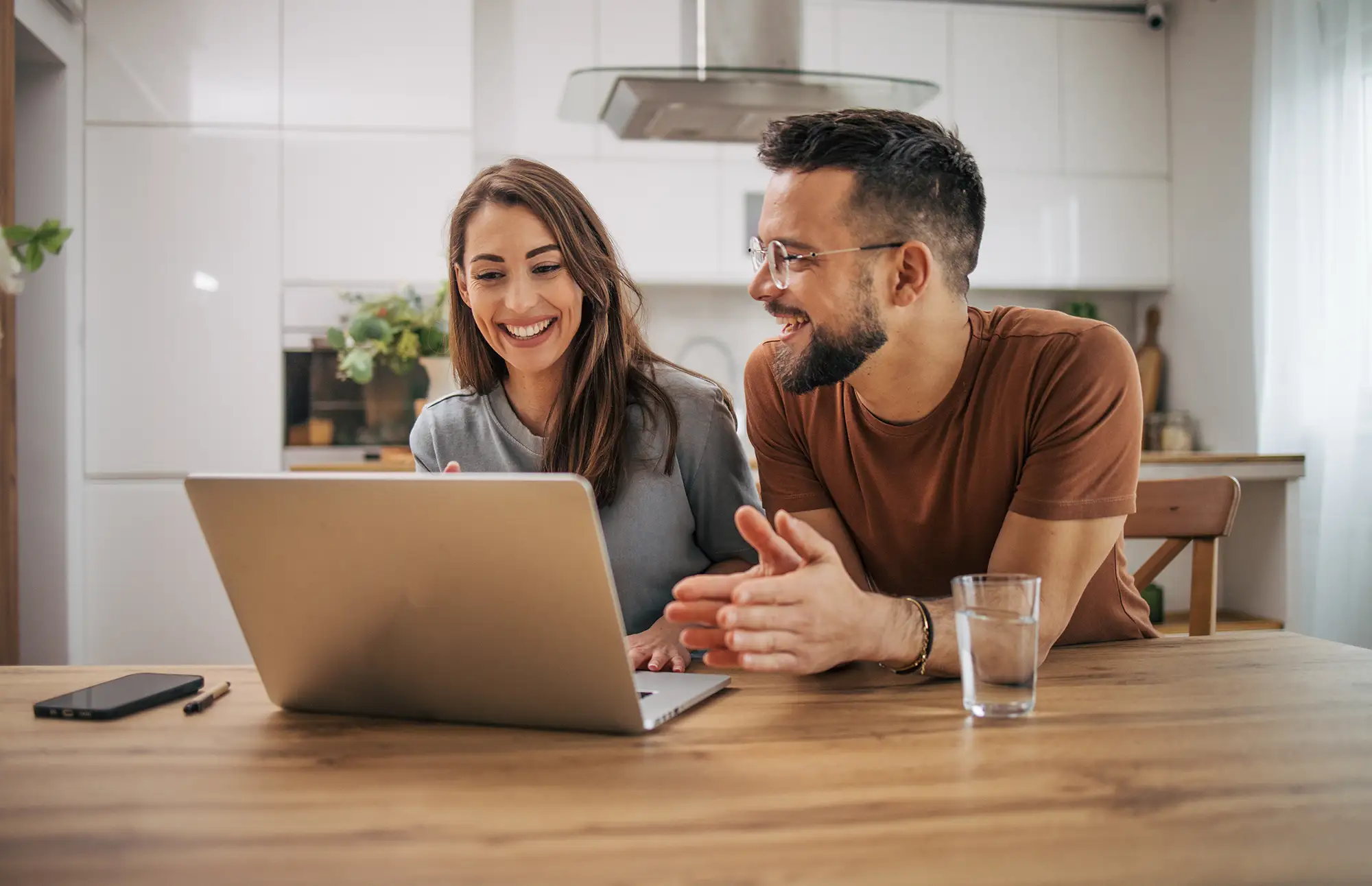 Happy couple sitting at their kitchen table looking at a laptop together