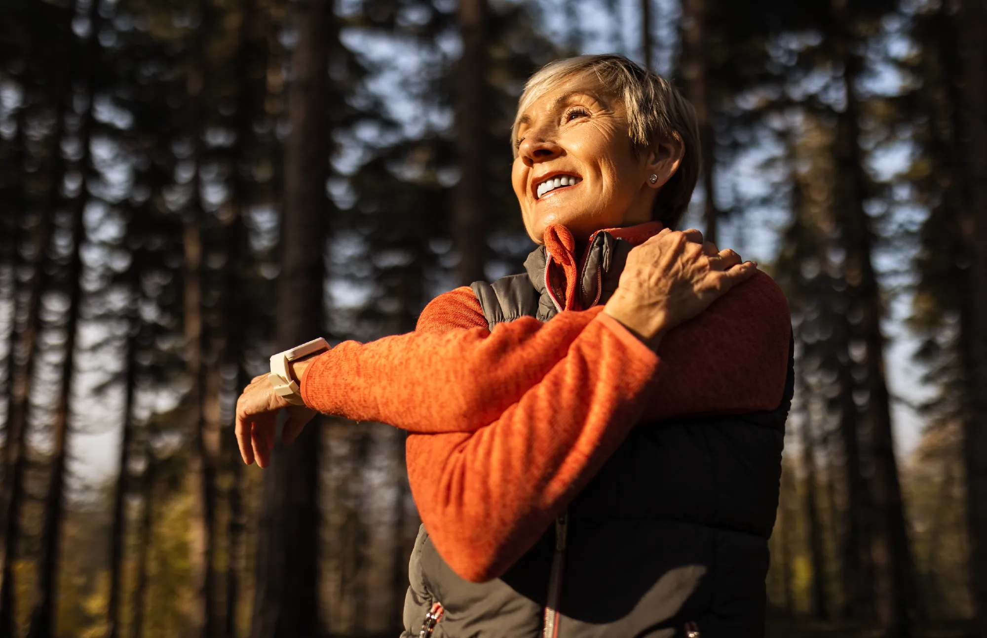 Smiling woman stretching outdoors in a forest.