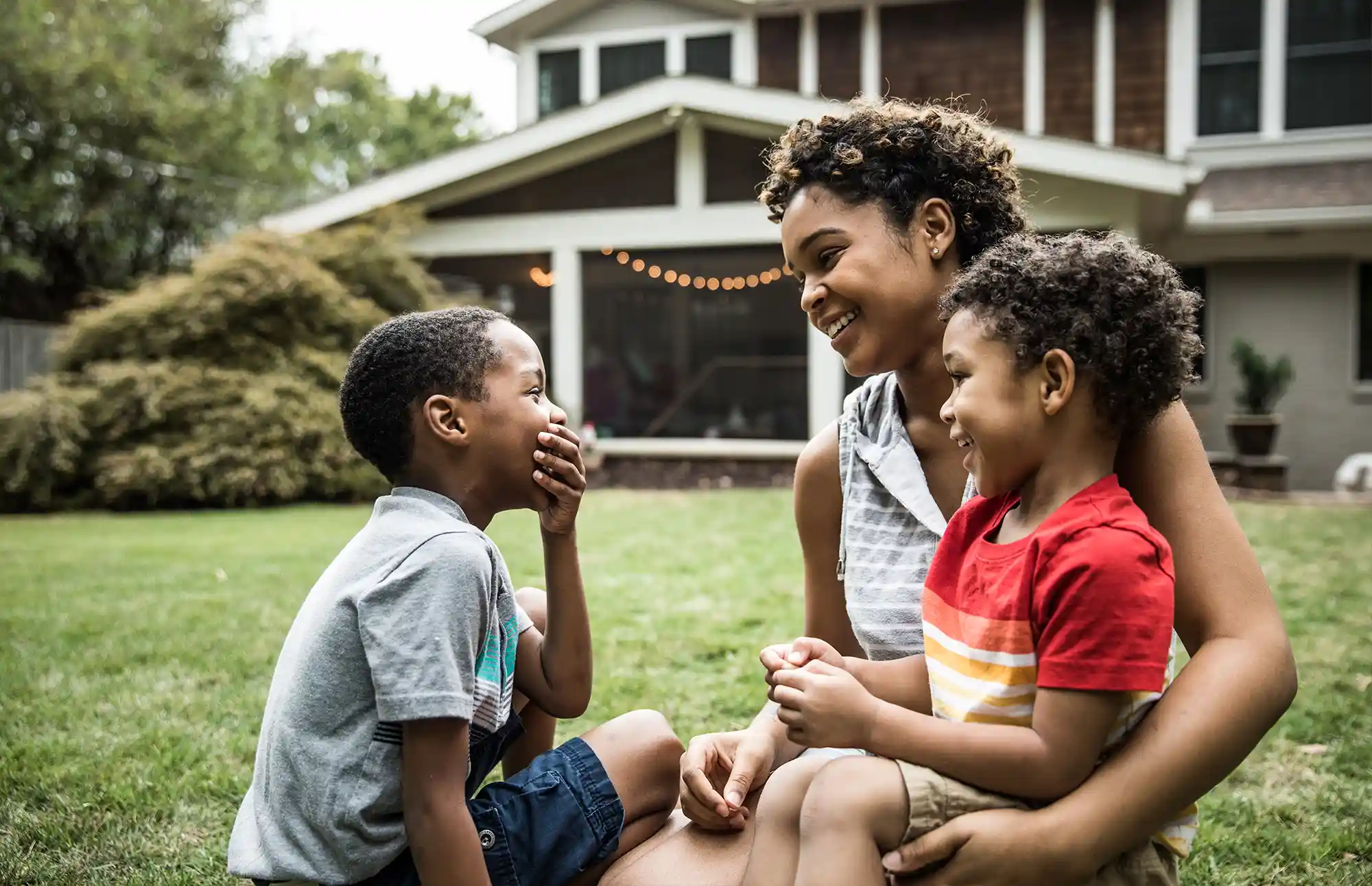 Mother and two young children sit and laugh in their backyard