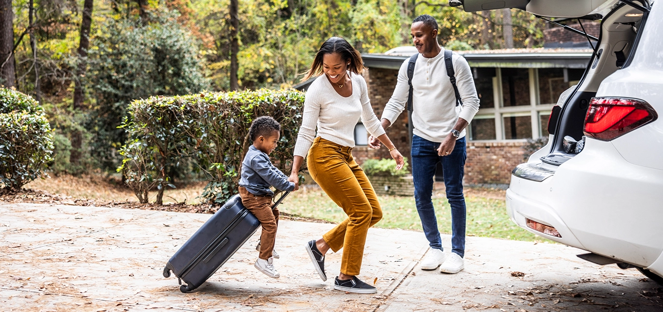 A family unloads luggage while a child pulls a suitcase outside a home.