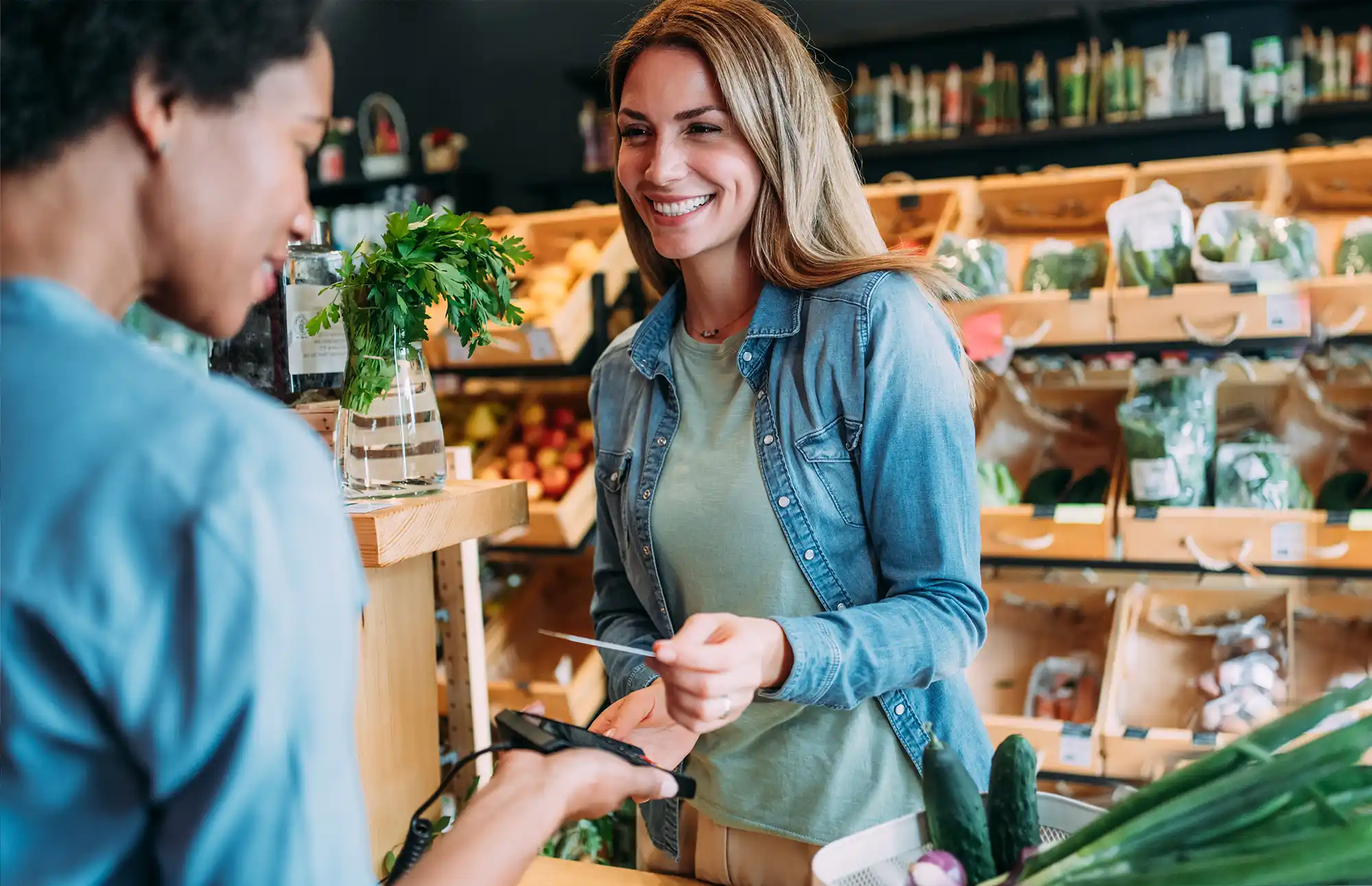 Woman smiles as she hands her credit card to a grocery store clerk