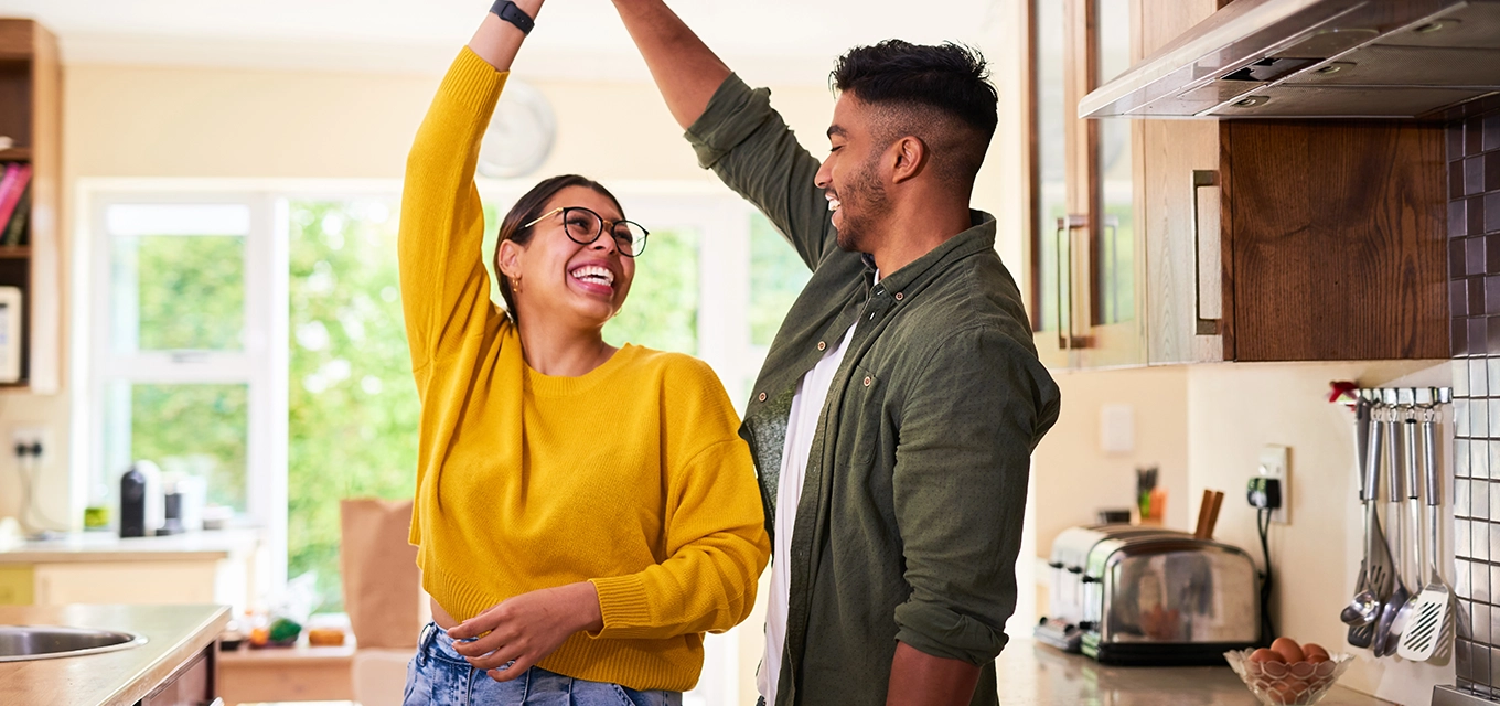 Two people smiling and high-fiving in a bright kitchen at home.