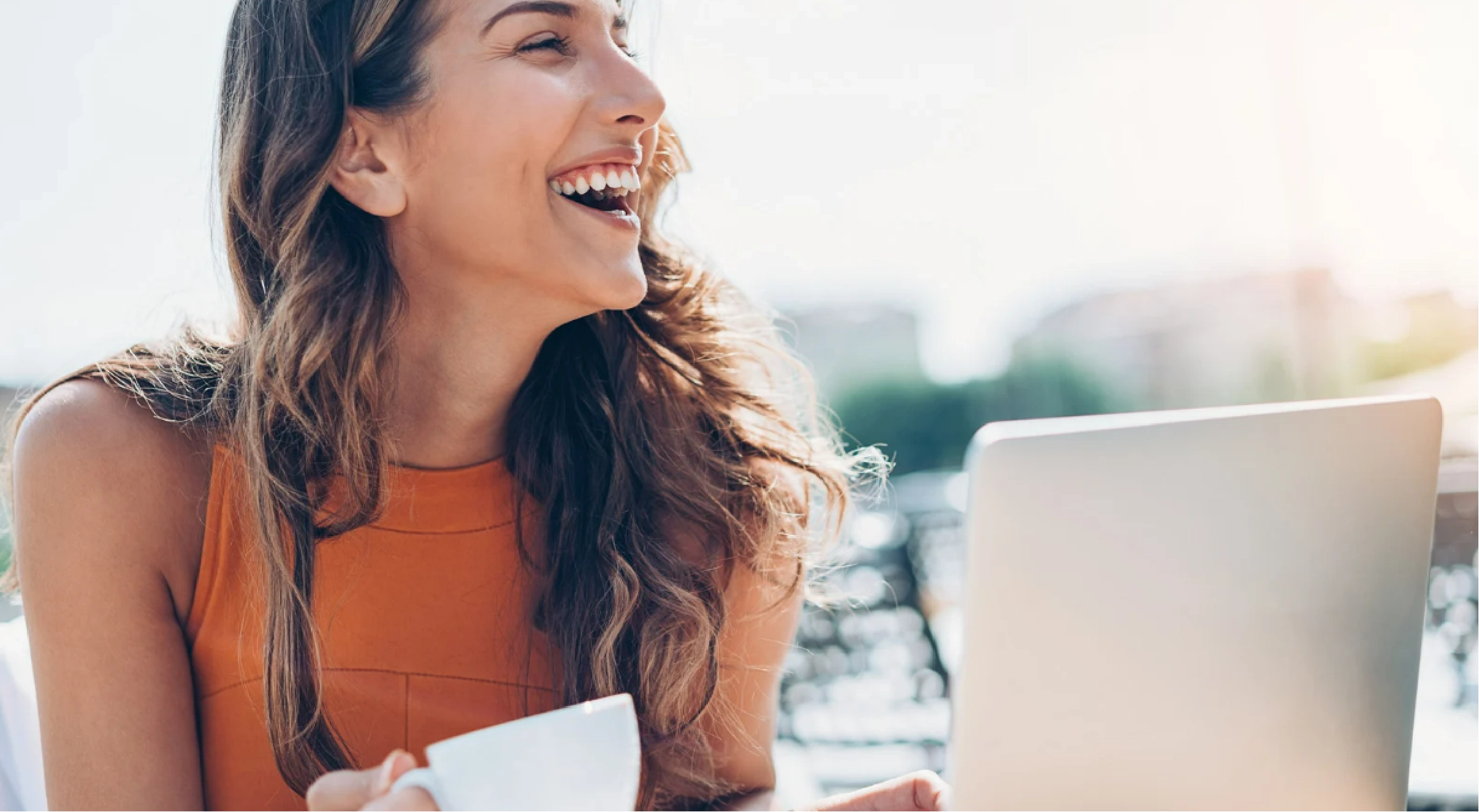 woman smiling outside holding coffee cup with laptop.