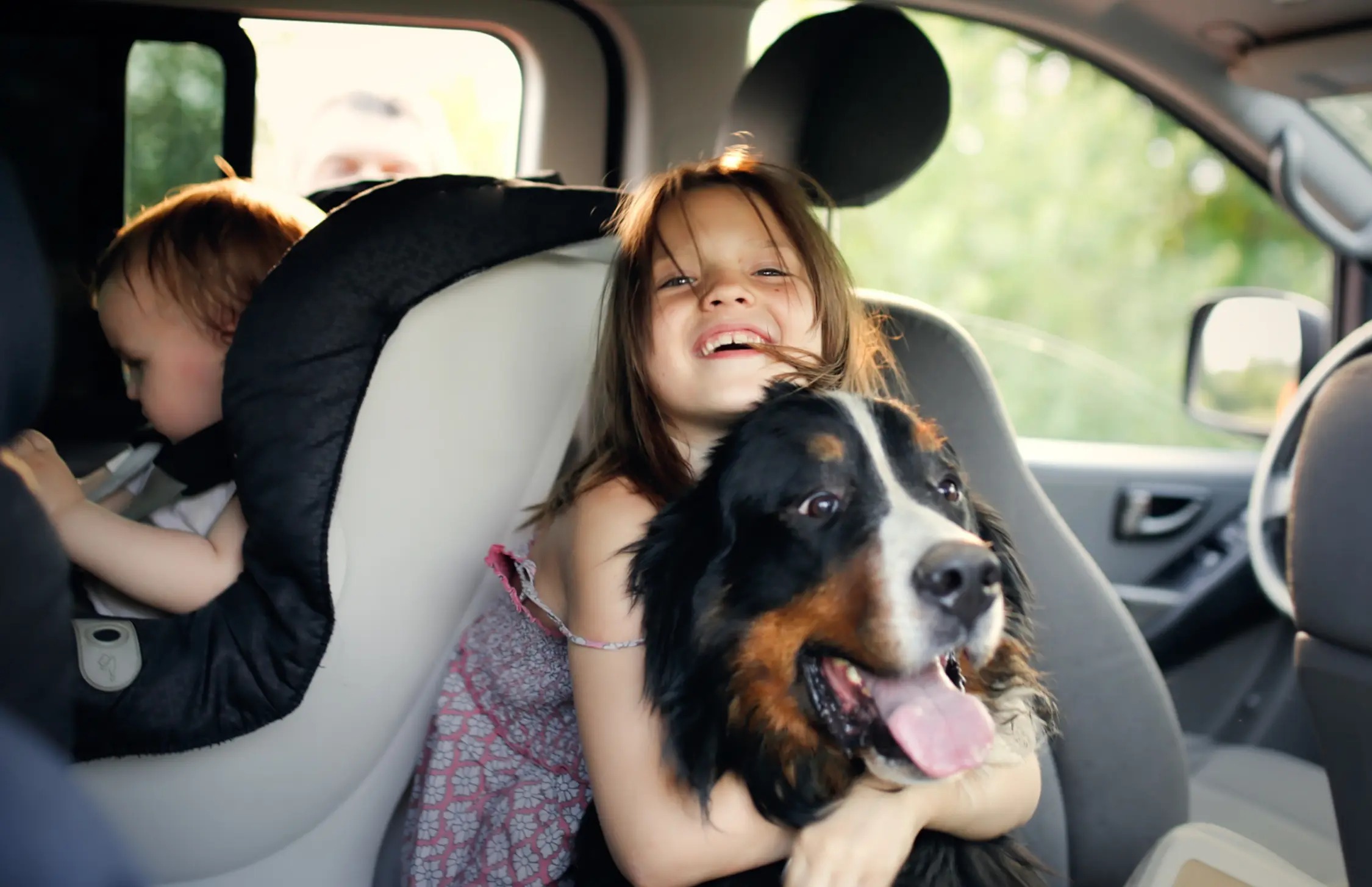 little girl hugging dog in a car
