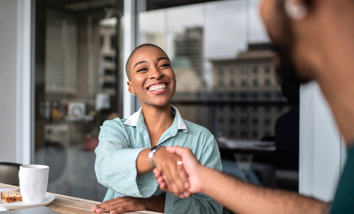 Woman shaking another person's hand over coffee