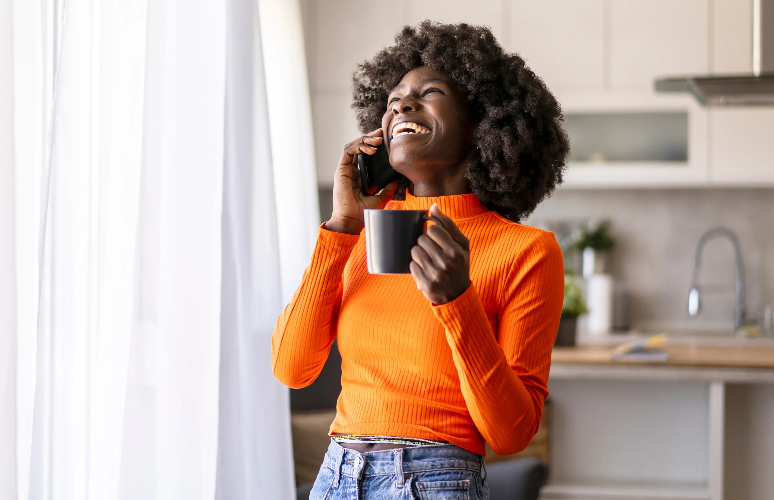 Woman laughs on the phone while holding a cup of coffee