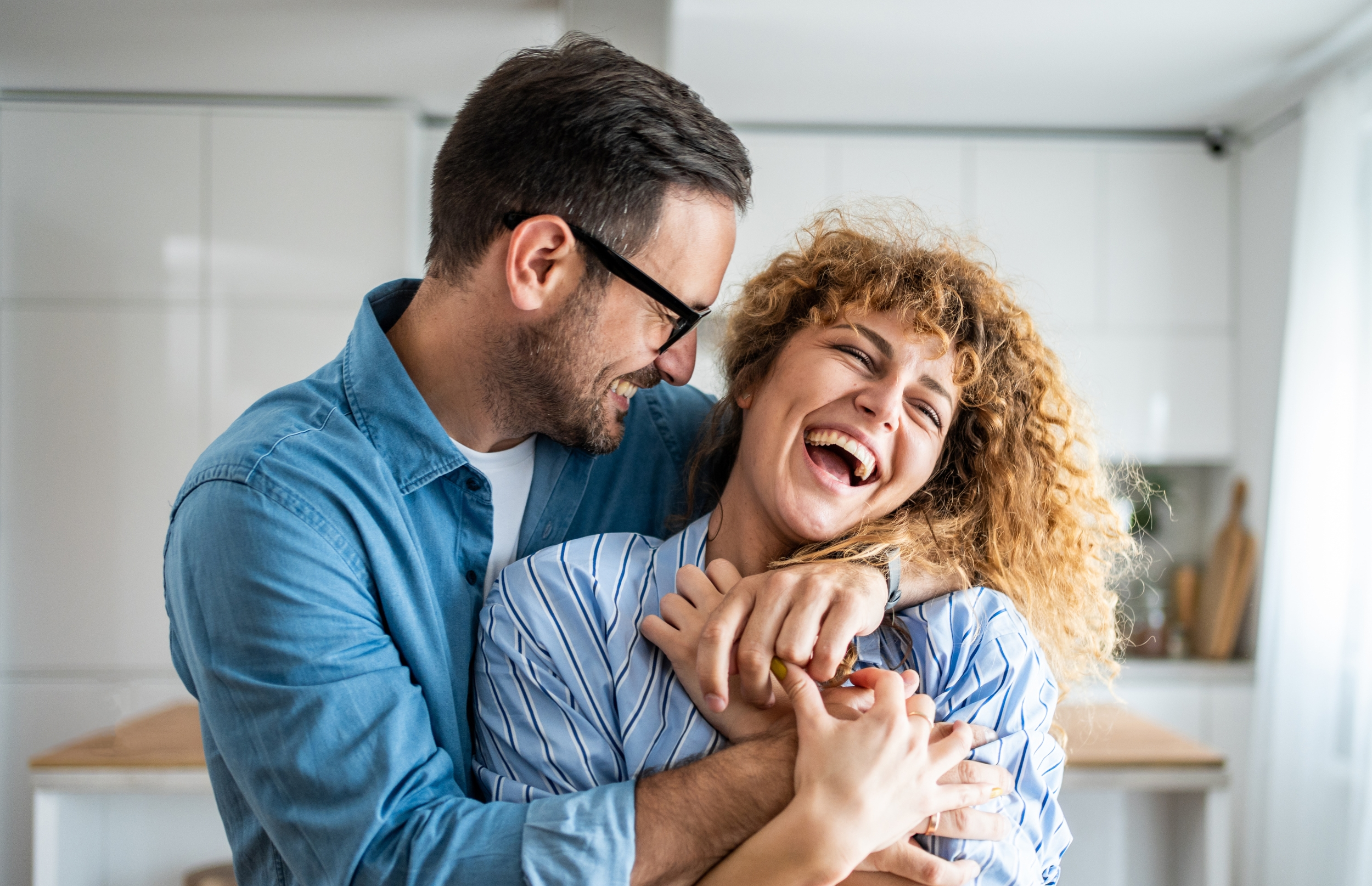 Couple laughs while sharing a hug in the kitchen