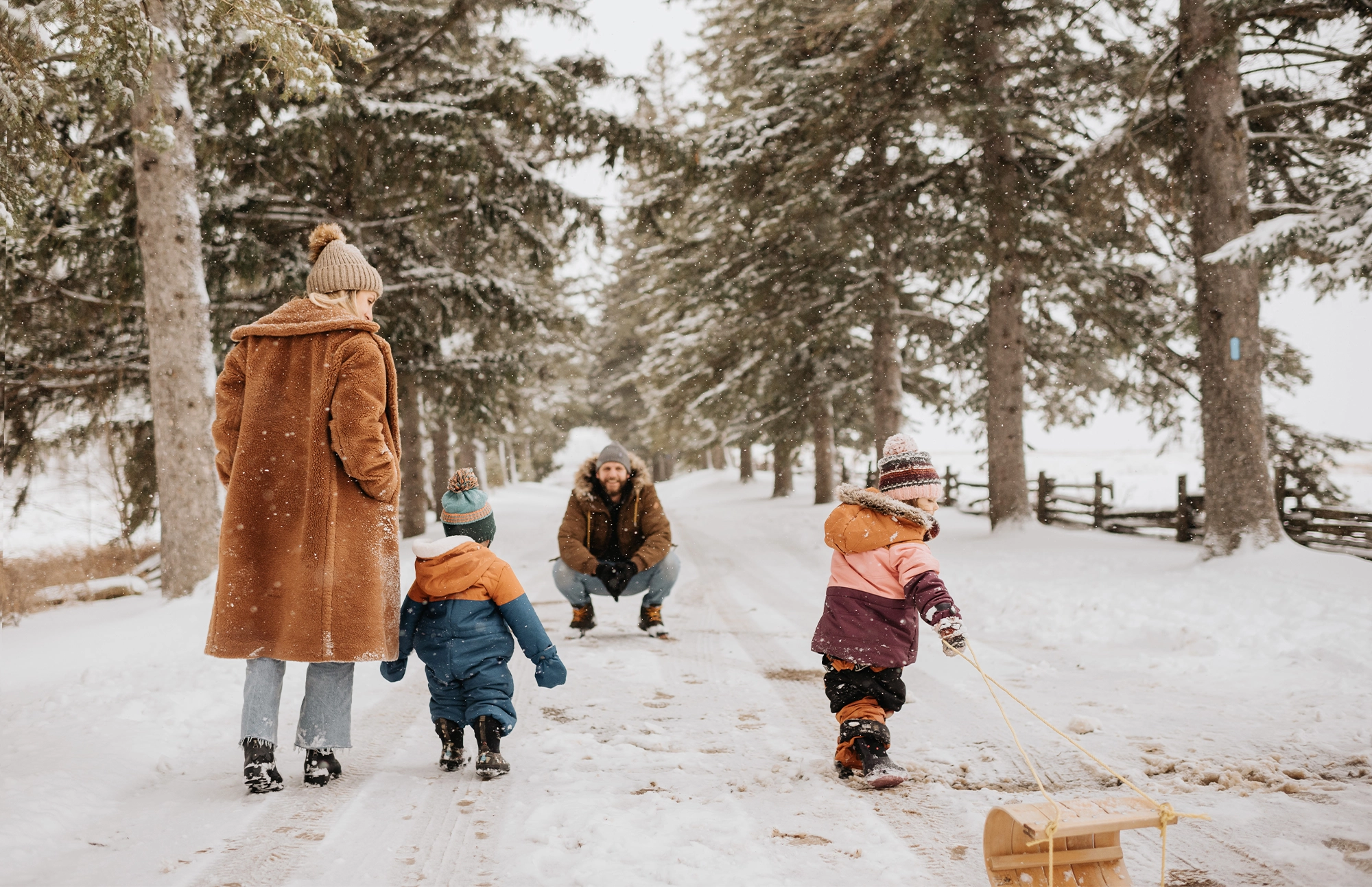 Family walking together on a snowy path while children play in the snow.